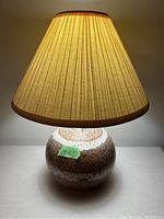 Front view of the vintage Maurice Chalvignac table lamp illuminated to show pleated lampshade and textured ceramic base with brown and white glaze.