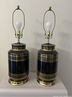 Pair of large black table lamps with gold decorative bands, no lampshades, showing full front view.