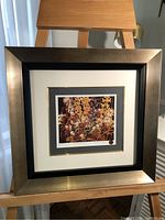 Framed artwork displayed on an easel showing full view of the print inside the dual-tone brass and black frame.