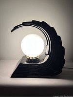 Side view of the black ceramic Art Deco revival wave table lamp illuminated with a frosted glass globe bulb.