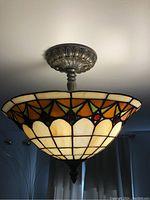 Full view of Tiffany style ceiling light fixture mounted on ceiling, showing stained glass bowl shade and decorative metal base.