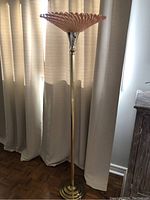 Vintage post modern brass torchiere floor lamp with decorative pink glass shade, shown unlit against curtain background.