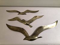 Three vintage brass bird wall art pieces arranged side by side on a flat surface, showing their size and design.