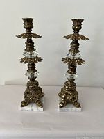 Front view of two ornate vintage candle holders showing detailed metal design, glass accents, and marble bases.
