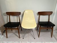 Front view of two wooden chairs with black vinyl seats and a yellow fiberglass chair with metal legs in between.