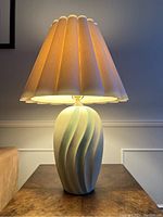 Full view of the vintage ceramic 1980s coastal style table lamp lit with scalloped beige fabric lampshade on a wooden table.