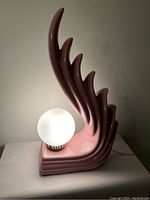 Front-left angle view of pink ceramic flame lamp with globe bulb illuminated and visible damage.