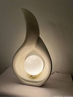 Front image of the beige ceramic flame-shaped lamp illuminated, showing the frosted globe bulb inside and the lamp's contours.