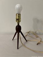Full view of small teak tripod egg lamp with bulb and cord