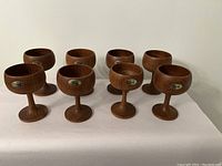Eight solid teak wood goblets arranged in two rows showing the full lot and labels.