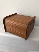Front view of the vintage solid teak box with closed tambour roll top door, showing smooth finish and integrated handle cut-outs on the side panel.