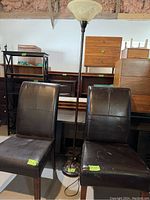 Two brown leather chairs and a floor lamp with a bowl-shaped frosted glass shade. Chairs show some wear on leather surfaces.