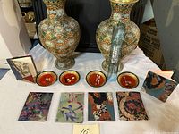 Full view of the lot including pair of cloisonné vases, four small round cloisonné plates, and four framed tiles/artworks laid on table.