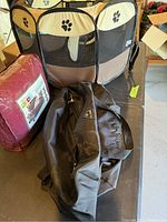 Photo showing the dog pen in brown and beige with black paw prints, the new sofa cover in packaging, and the black bag.