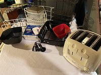 White kitchen items including wire racks, plastic strainers, measuring spoons, and a white toaster with two knobs.