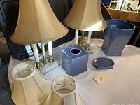 Image showing two lamps with marble bases, two spare lamp shades and four blue bathroom accessories on a surface in garage setting.