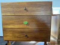 Front view of mid-century wooden dresser showing 3 drawers with round metal knobs and wood grain finish.