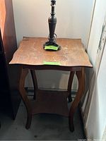 Photo showing oak side table with scalloped edge top and curved legs, including a black table lamp on top.
