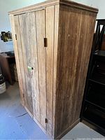 Side angle view of tall vintage wooden cabinet showing vertical plank construction and weathered surface.