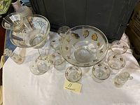 Complete vintage glass punch bowl set with leaf motif including bowl, ladle, cups, and bottle displayed on surface