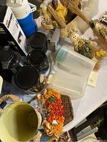 Photo showing black kitchen storage jars, plastic storage containers, blue thermos, fall flowers, woven placemats, and ceramic wastebasket