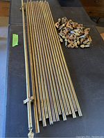 Stack of brass stair rods with pineapple finials and many mounting brackets on black table surface.