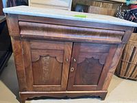 Front view of walnut/mahogany night stand showcasing two paneled doors with scalloped design, a drawer above, and original marble top.