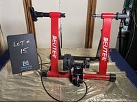 Side front view of the red Deuter stationary bike trainer stand showing the frame, resistance unit, and cable laid on ground.