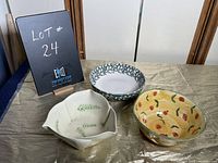 Three ceramic bowls on a tablecloth: a white bowl with fern leaf pattern and three rim points, a round bowl with green leaf pattern, and a cherry-patterned bowl with yellow interior.