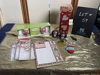 Wide view of Christmas assortment including mugs, decorative box, greeting cards, ornament balls, and mitten pouch