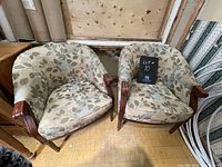 Wide view of two upholstered club chairs with green leaf patterned fabric, wooden arms, and wooden Queen Anne style legs set side by side.