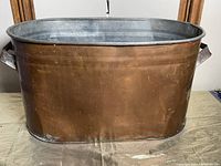 Front view of the oval copper planter showing its shape, metal finish, and handles on each side.