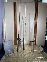 Three fishing poles standing upright with reels and handles visible, displayed against a plain background.