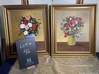 Pair of floral still life paintings in gold colored frames, side by side, showing front views of both paintings.