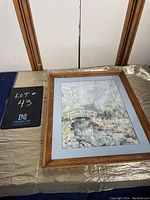 Framed watercolour painting showing a landscape with a bridge, placed on a gold fabric with wooden frame borders visible