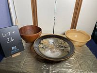Three large bowls displayed together: a wooden bowl, a large ceramic bowl with multicolor glaze, and a yellow ceramic bowl
