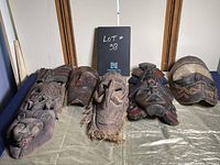 Collection of eight African themed masks displayed on a green fabric with handwritten sign behind showing lot number