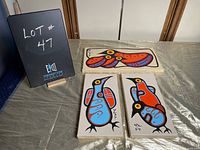 Three paintings displayed on table: two vertical and one horizontal.