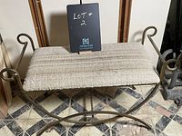 Front angle view of the gold iron frame bench with upholstered seat showing the scroll design on arms and woven fabric on seat cushion.