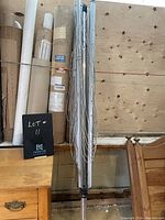 Full view of the folded clothesline showing the metal frame and multiple clotheslines hanging down, next to wooden furniture and cardboard rolls.