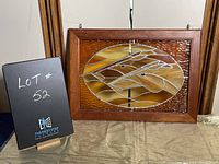 Framed stained glass artwork showing abstract horses in warm brown and amber tones, set in wooden frame with wire hangers.