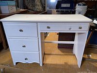 Front view of vintage wooden desk painted white, showing four drawers with brass handles and some wear marks on surface.