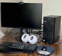 Full setup showing Acer desktop tower, HP 27" monitor with Logitech webcam, Microsoft keyboard, Acer wired mouse, Creative speakers on wood table
