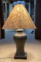Chinese vase table lamp showing ceramic vase base on wood square base and textured natural fiber shade illuminated.
