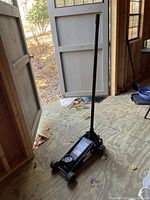 Full view of the black Craftsman floor jack with handle inside a wooden shed, showing overall condition and size.