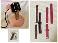 Fitbit Luxe tracker on pink charging stand with rose-gold metal band and fold-over clasp next to multiple replacement bands and a band adjustment kit seen below.