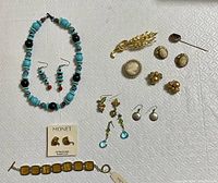 Full view of all jewelry items arranged on a white patterned fabric, showing necklace, earrings, Monet bracelet and earrings, and vintage brooches, rings, and pins.