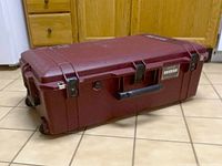 View of the closed dark red Pelican hard travel case showing exterior features including handle, latches, wheels, and TSA lock key hole.