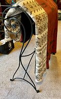 Side view of metal quilt rack displaying decorative scroll work on ends and two throws draped over it.