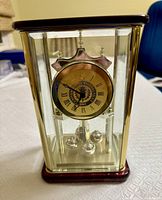 Front view of table top pendulum clock showing glass case, clock face with Roman numerals, and revolving pendulum below